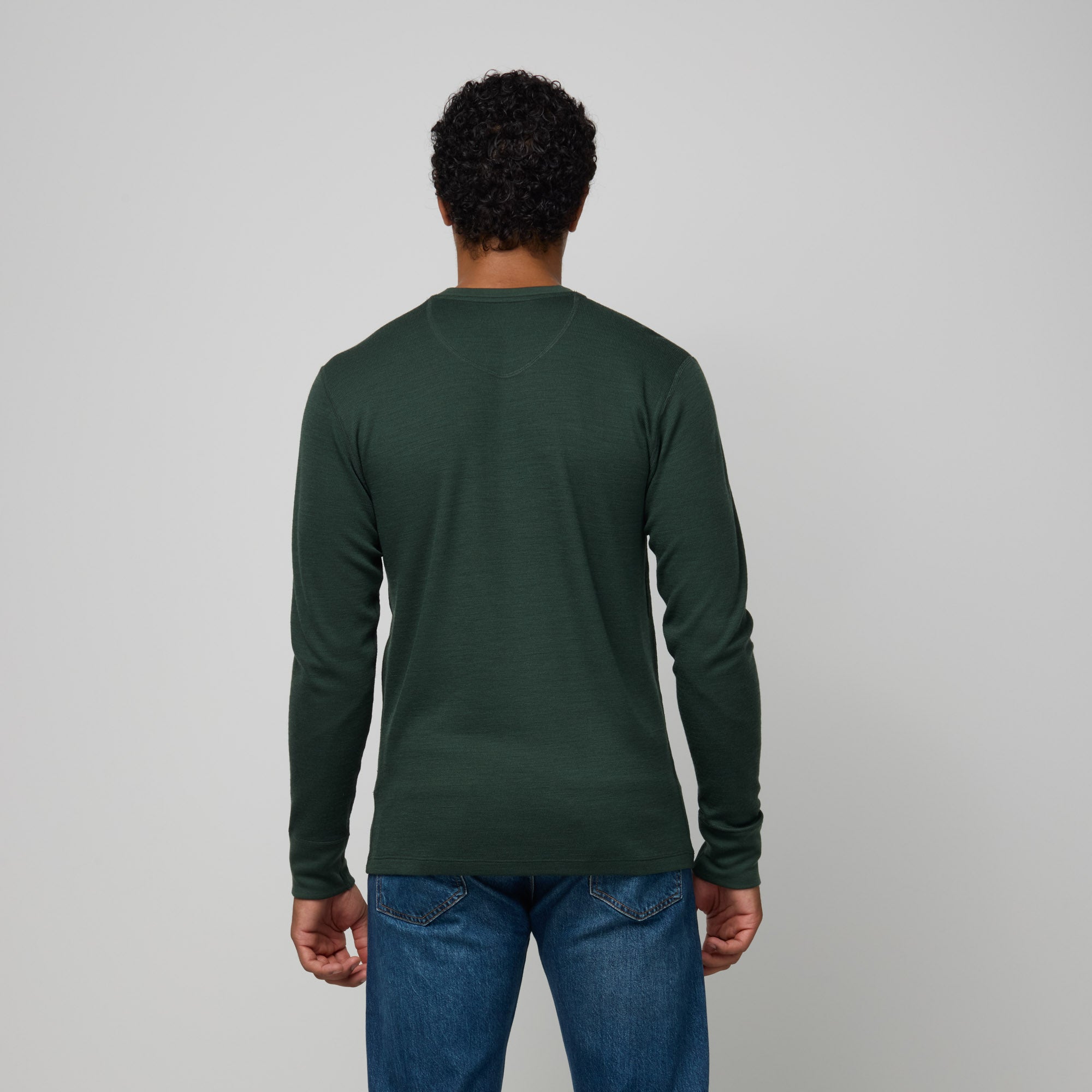 Model wearing merino wool Waffle Henley in Hunter Green, a dark green with blue undertones. This is a long sleeve, crew neck henley shirt available in sizes XS-XXL.