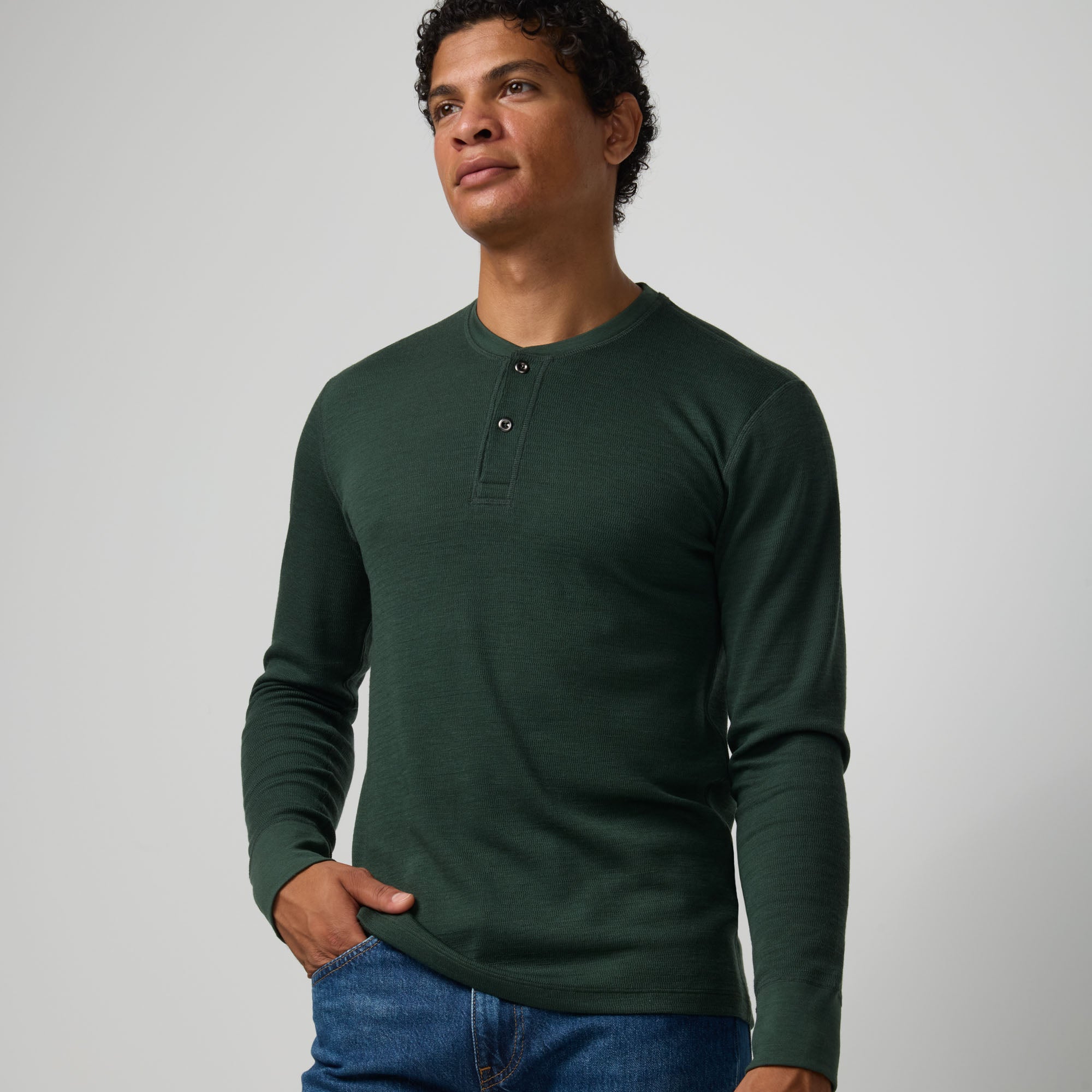 Model wearing merino wool Waffle Henley in Hunter Green, a dark green with blue undertones. This is a long sleeve, crew neck henley shirt available in sizes XS-XXL.