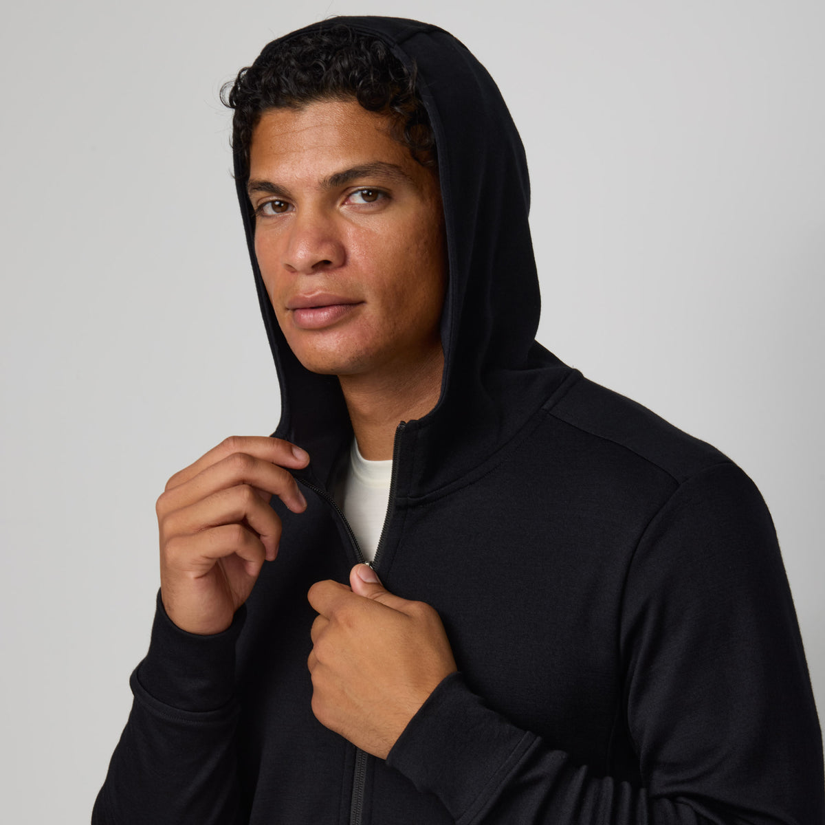 Model wearing merino wool Interlock Travel Hoodie in Black. This is a midweight full-zip hoodie available in sizes XS-XXL.