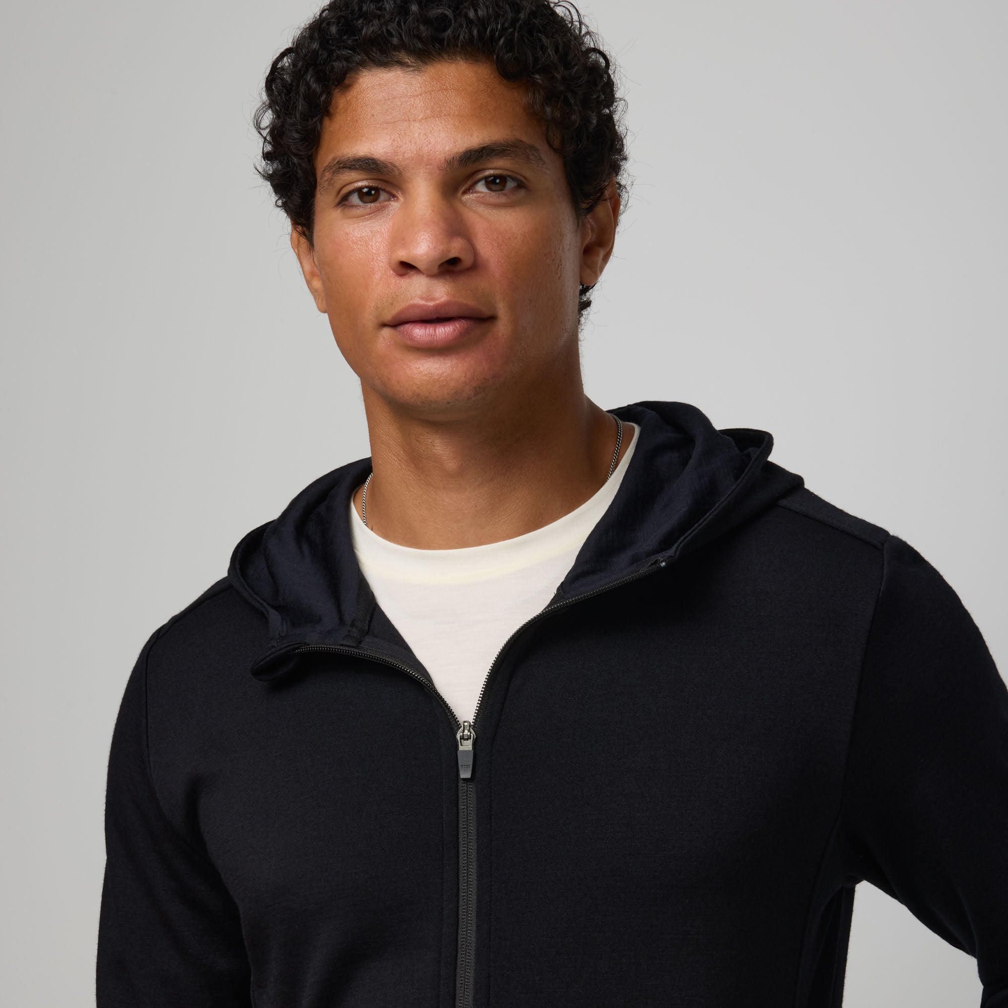 Model wearing merino wool Interlock Travel Hoodie in Black. This is a midweight full-zip hoodie available in sizes XS-XXL.