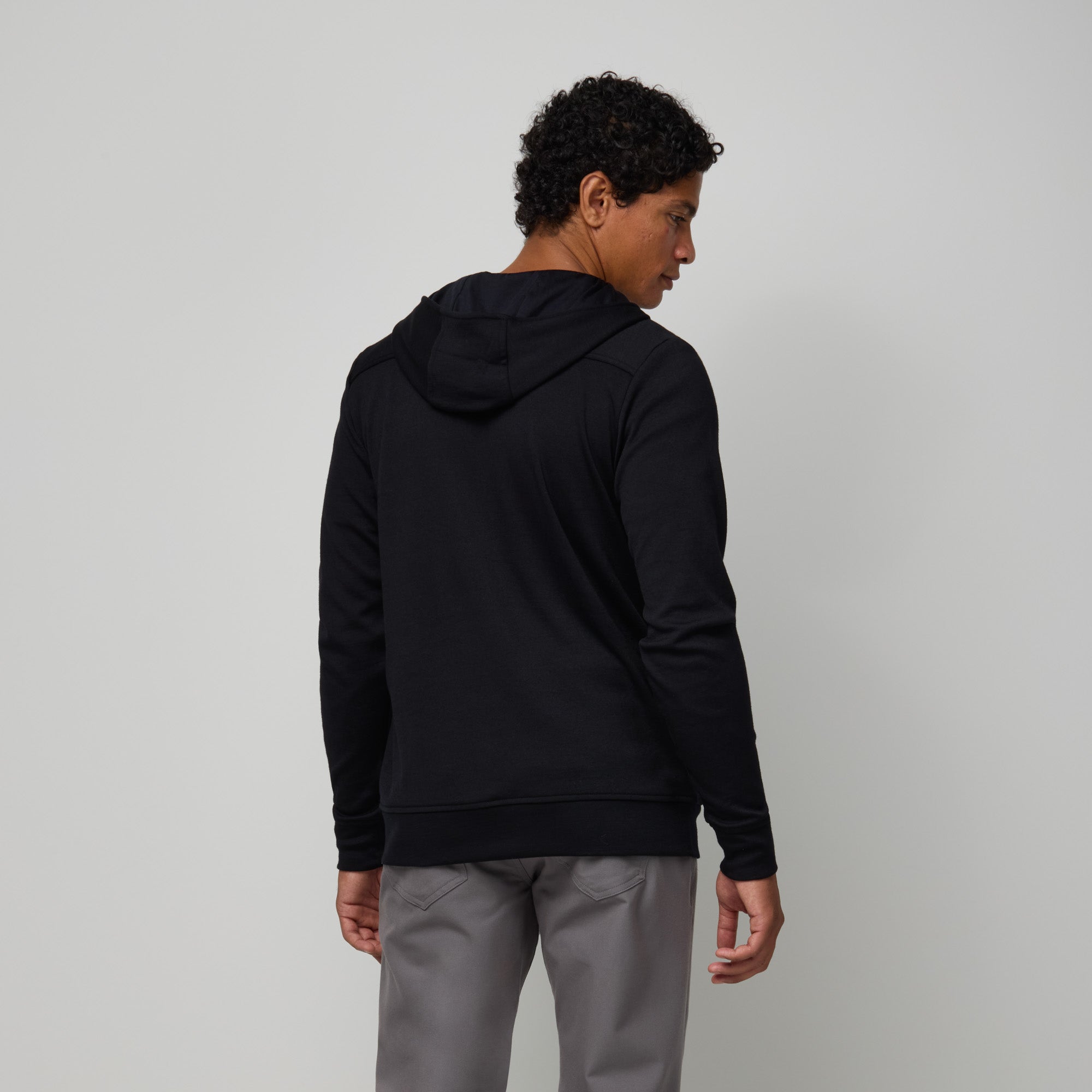 Model wearing merino wool Interlock Travel Hoodie in Black. This is a midweight full-zip hoodie available in sizes XS-XXL.