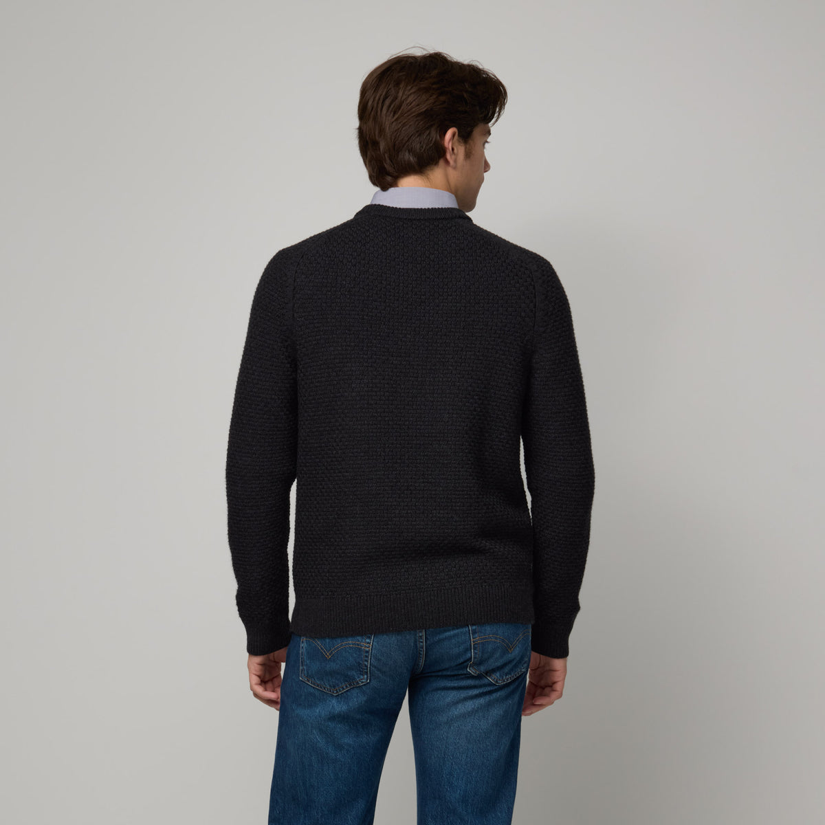 Model wearing 100% merino wool Textured Crew Neck Sweater in Black Heather, a dark gray color. This is a knit available in sizes S-XXL.