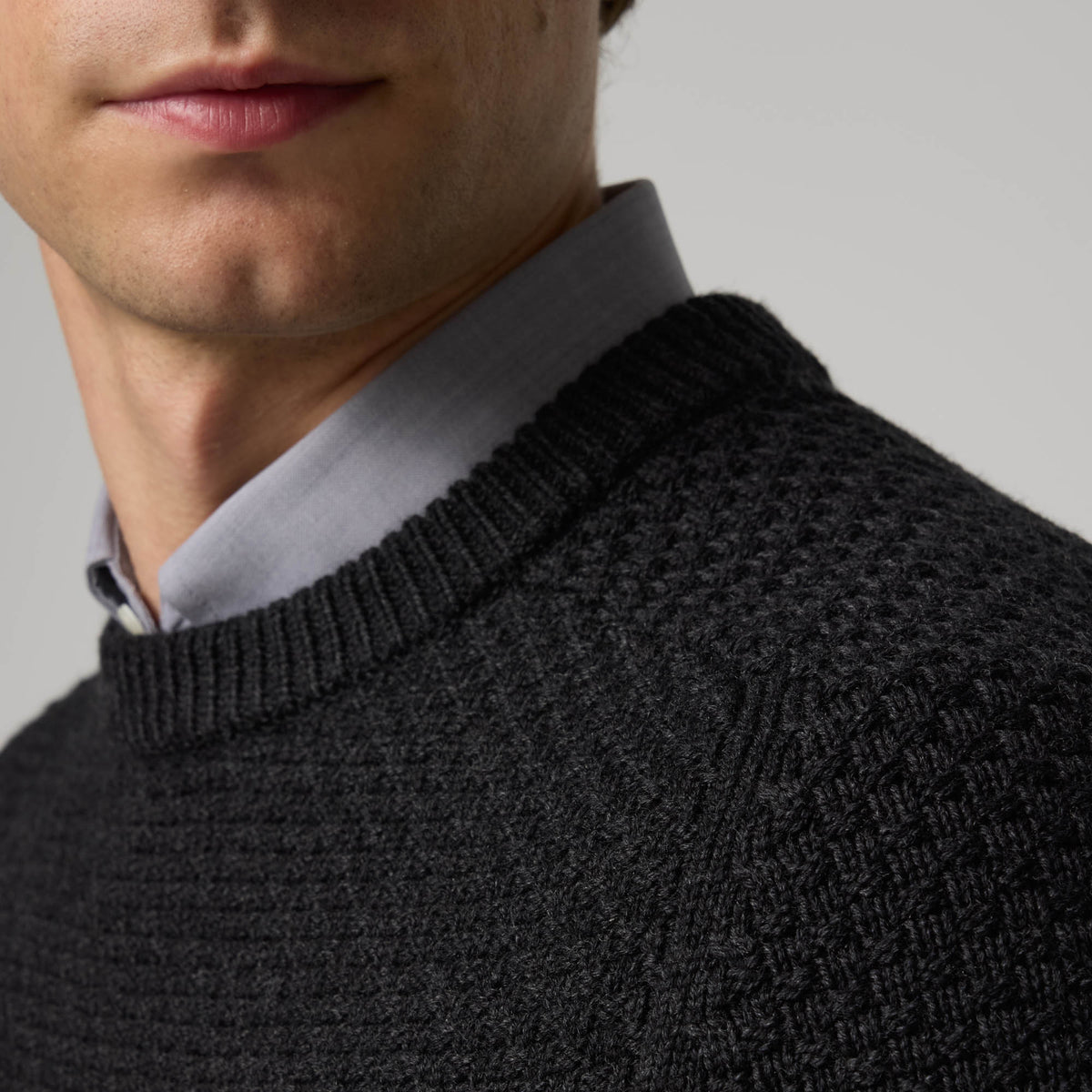 Model wearing 100% merino wool Textured Crew Neck Sweater in Black Heather, a dark gray color. This is a knit available in sizes S-XXL.